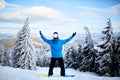 Snowboarder raised his arms and hands to the sky at ski resort. Man climbed a mountain top through forest for