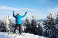 Snowboarder raised his arms and hands to the sky at ski resort. Man climbed a mountain top through forest for