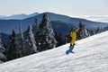 Snowboarder riding down the slopes wearing yellow mono suit on sunny day with fresh snow.