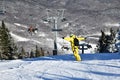 Snowboarder riding down the slopes wearing yellow mono suit on sunny day with fresh snow.