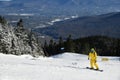 Snowboarder riding down the slopes wearing yellow mono suit on sunny day with fresh snow.