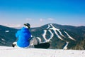 Snowboarder sitting on snow against mountains