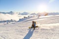 A snowboarder in a ski mask and a backpack is riding on a snow-covered slope leaving behind a snow powder against the Royalty Free Stock Photo