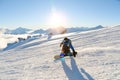 A snowboarder in a ski mask and a backpack is riding on a snow-covered slope leaving behind a snow powder against the Royalty Free Stock Photo