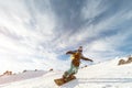 A snowboarder in a ski mask and a backpack is riding on a snow-covered slope leaving behind a snow powder against the Royalty Free Stock Photo