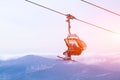 Snowboarder and skier in professional outfit climb up cable car lift up mountains on background of sky, sun and mountain peaks.