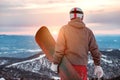 Snowboarder stands with snowboard against sunset