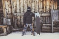 Snowboarder wearing black jacket, mask with snowboard close authentic wooden house. Horizontal. Royalty Free Stock Photo