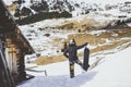 Snowboarder wearing black jacket, mask with snowboard close authentic wooden house.Man looking at panoramic mountans Royalty Free Stock Photo