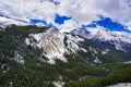 Snow capped Canada`s Rockies mountain during a summer day contrasting with a bright blue sky and white clouds