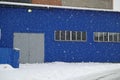 Snowfall on the background of an industrial warehouse of blue metal
