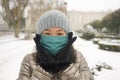 Snowfall in covid19 time - young happy and attractive Asian Chinese woman in winter hat and mask at beautiful city park playing Royalty Free Stock Photo