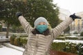 Snowfall in covid19 time - young happy and attractive Asian Chinese woman in winter hat and mask at beautiful city park playing Royalty Free Stock Photo