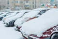 Snowfall and snow-covered cars stand in the courtyard of a multi-storey building.