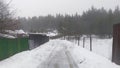 After the snowfall snow lies on the ground and roofs of houses. Along the street there are metal and wooden fences and electricity