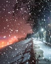 Snowfall in a winter park at night with glowing lanterns, view to road with car motion, pavement and trees in foggy weather Royalty Free Stock Photo