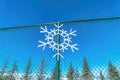 Snowflake ornament hanging on a green chain link fence against clear blue sky Royalty Free Stock Photo