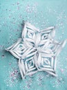 Snowflake from paper with colorful confetti on trendy mint colored background. Simple holiday concept. Winter festive backdrop.