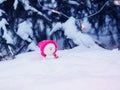 card with a festive cute toy snowman in a bright pink cap sitting in a snowdrift with a gift under the Christmas tree in Royalty Free Stock Photo