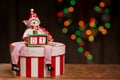 A snowman figure is sitting on a decorated decoupage box and holding a smaller box with two cubes forming a number one.