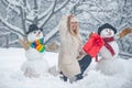 Snowman and funny girl in the snow. Girl playing with Snowman - isolated on snow background. Joyful Beauty young woman Royalty Free Stock Photo