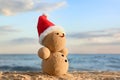 Snowman made of sand with Santa hat on beach. Christmas vacation