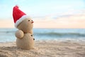 Snowman made of sand with Santa hat on beach near sea, space for text.
