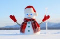 The snowman in plaid scarf, red hat, gloves and icicle in the hand. Nice landscape with the mountains on the background. Royalty Free Stock Photo