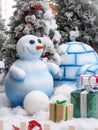 A snowman standing against Christmas trees surrounded with gift boxes. Royalty Free Stock Photo