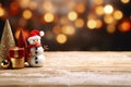 Snowman toy and Christmas ornament on wooden table with snow and blurred city light bokeh background, Christmas background. Royalty Free Stock Photo