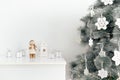 Snowman, white candlestick and white gift boxes on a white table against the background of a Christmas tree