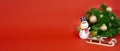 A snowman, a wooden sled, decorated fir branches on a red background with a place to copy. Banner