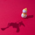 A snowman with a yellow scarf and a hat and a shadow of a witch on a broom flying towards him on a red background and copy space. Royalty Free Stock Photo