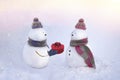 Snowmen in love wearing winter hats, scarves on a white background in pink and blue colors. Boy giving a gift to his