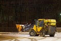 A snowplow clears the street of snow at night.