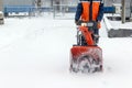 A snowplow driven by a person moves along the road and dumps snow into it. A worker removes snow with a small snow blower. Royalty Free Stock Photo