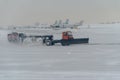 Snowplow removing snow from runways and roads in airport during snow storm, view through window