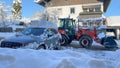 A snowplow tractor clears a road while a snow-covered car is parking in the foreground in the winter season Royalty Free Stock Photo