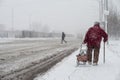 A snowstorm in the city. An elderly woman with a cane and a bag on wheels goes along the road Royalty Free Stock Photo