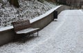 Snowy benches near the supporting concrete gray wall in the park. Paving and metal low fences protect ornamental flower beds from