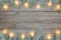 Snowy christmas tree branches and glowing star garlands of wooden background
