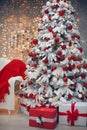 Snowy Christmas tree with red gifts before bokeh lights and wreath decoration on the wall with present boxes in the comfy room in Royalty Free Stock Photo