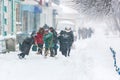 A snowy city street during a heavy snowfall. People with snow shovels clear sidewalks in winter during snowfall. Winter time in