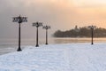 Snowy embankment along the misty river with lanterns at the foggy sunrise - winter landscape. I