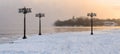 Snowy embankment along the misty river with lanterns at the foggy sunrise - winter landscape. II