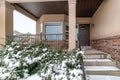 Snowy evergreens beside stairs that leads to porch of home with front bay window