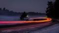 Snowy foggy forest road with car tail lights.