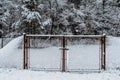 Snowy frozen metal fence and gate,trees in backround.Winter snowy weather.Old forest fence and entrance door with smaller holes Royalty Free Stock Photo