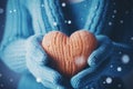 Snowy heart held by female hands in warm knitted gloves