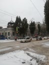 a snowy intersection with cars trees and buildings and houses on a snowy day